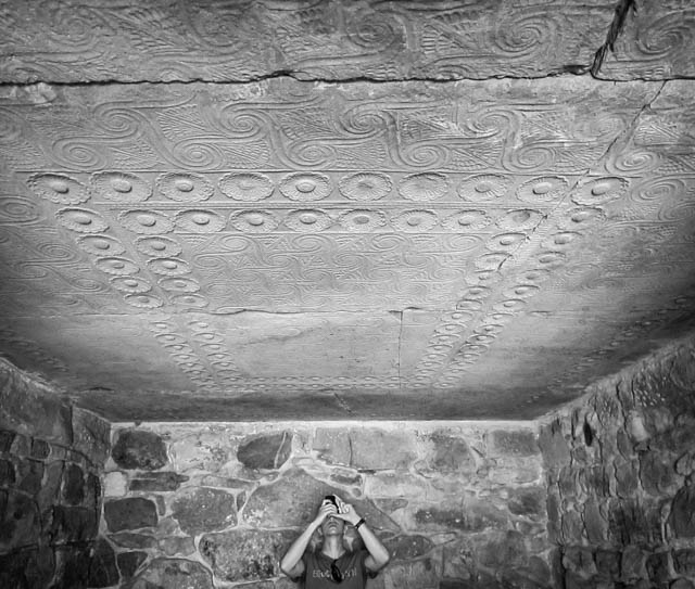 Orchomenos, Greece, by Molly Allen. The image shows Matt Peebles (PhD Columbia, art history) taking a picture of the ornately decorated ceiling of the chamber tomb which juts out from the northeast side of the "Tomb of Minyas." The ceiling contains relief decoration with spirals, rosettes and papyrus flowers, etched into enormous limestone blocks. The tomb was plundered in antiquity but the tholos structure was intact at least until the 2nd century AD, when Pausanias wrote about its impressive structure (9.38.2-3). 